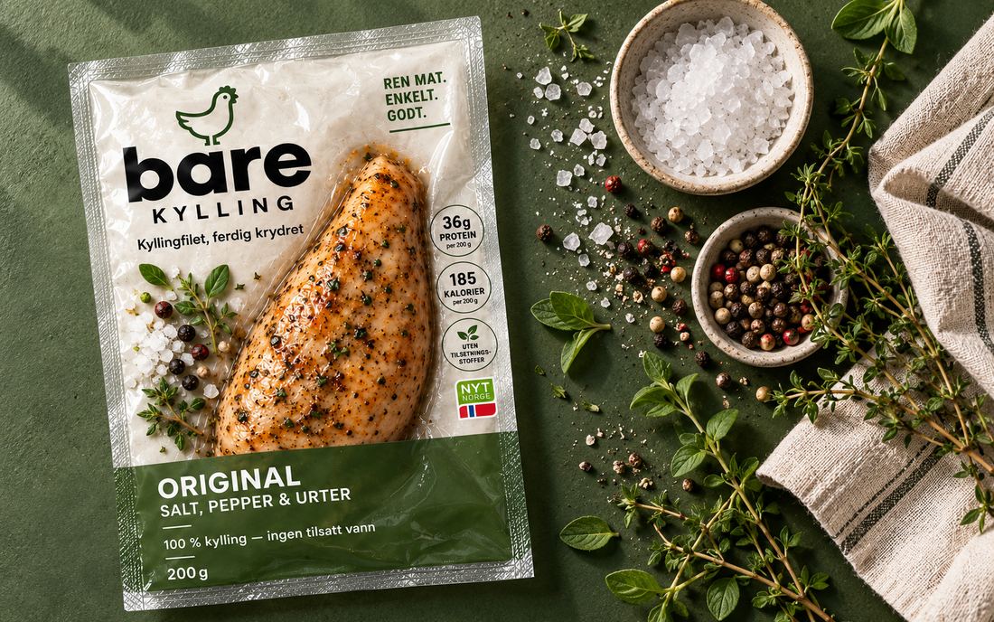 En pakke Bare Kylling Original på mørkegrønn bakgrunn, med grovt salt, pepperkorn og friske urter ved siden av.