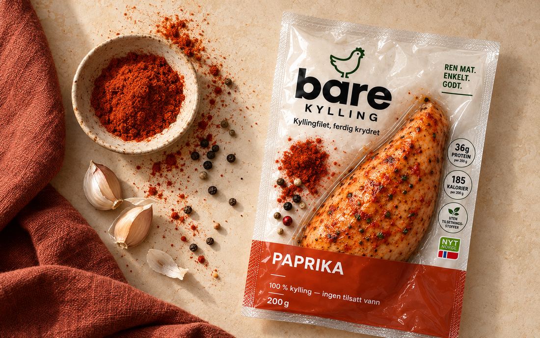 En pakke Bare Kylling Sweet Paprika på en lys benk, med en skål paprikapulver, pepperkorn og hvitløk ved siden av.